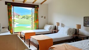 A hotel room with two beds, a small table, and a chair. There is a window with curtains, and a view of a pool and greenery outside. - Casa rodeada de naturaleza en Villeta (Villeta)