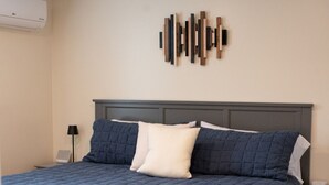A neatly made bed with a dark blue quilt, a white pillow, and two dark blue pillows. There is a wall-mounted artwork above the bed. - The Nautilus at JS Hubbs Guest House (Hammondsport)