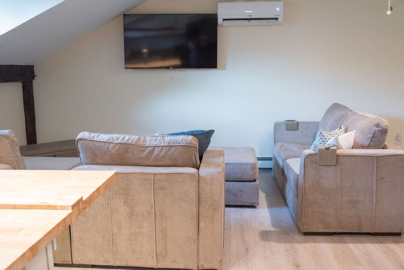 A modern living room with a wooden dining table, two beige sofas, and a mounted flat-screen TV.
