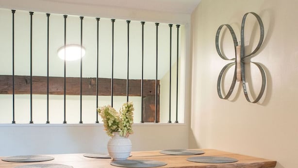 Un comedor con mesa de madera, barandales de metal y un adorno decorativo con forma de mariposa en la pared.