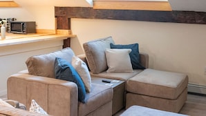 Un espacio habitable estilo loft acogedor con sofá seccional, una kitchenette pequeña y un tragaluz.