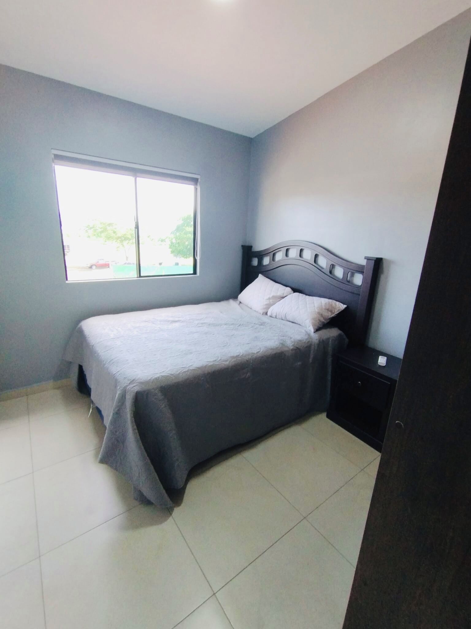Een slaapkamer met een bed, nachtkastje en raam.