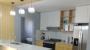 Une cuisine moderne dotée d’un îlot central, d’appareils électroménagers intégrés et de luminaires suspendus.