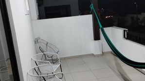 Un balcon doté d’un sol carrelé de carreaux blancs, d’un hamac vert et de trois chaises en métal blanc.