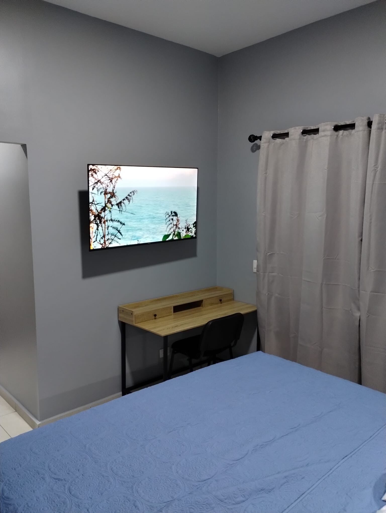 Ein Schlafzimmer mit Bett, Schreibtisch, Fernseher an der Wand und einem Vorhang.