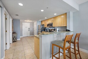 A kitchen with wooden cabinets, a stainless steel refrigerator, a microwave, and a granite countertop.