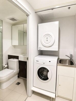 A compact bathroom with a toilet, a washing machine, a sink, and a mirror.