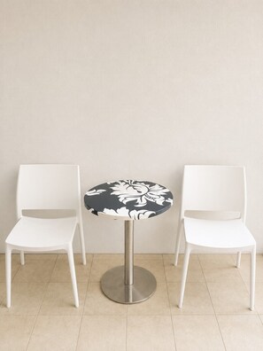 A small round table with a black and white floral pattern, flanked by two white chairs, against a plain wall.