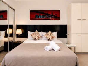 Habitación de hotel con cama, mesita de noche con lámpara, un cuadro en la pared y un armario.