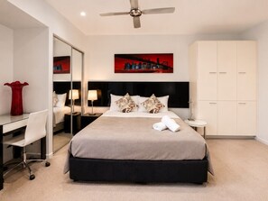 A hotel room with a bed, desk, chair, wardrobe, and a ceiling fan.