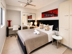 Habitación de hotel con cama, escritorio, silla, mesa redonda, espejo y un cuadro de un paisaje urbano.