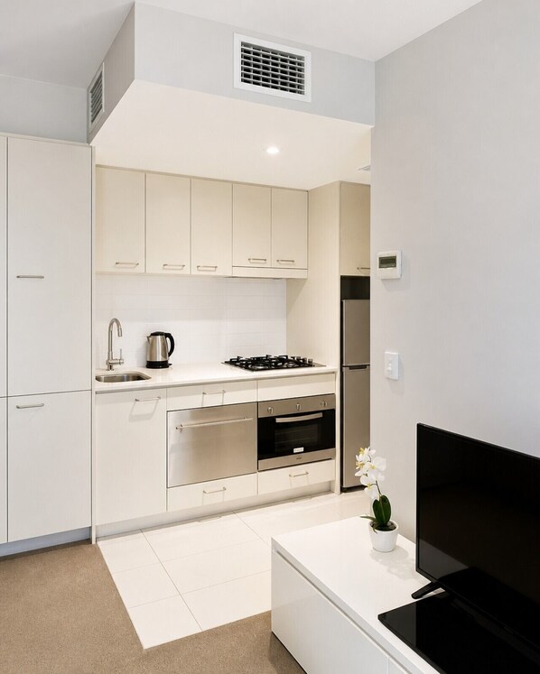 A modern kitchen with white cabinets, a gas stove, an oven, a sink, and a black TV on a white countertop.