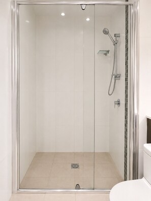A glass-enclosed shower with a handheld showerhead and a wall-mounted faucet.
