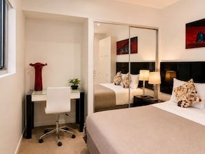 Una habitación de hotel con cama, escritorio, silla, espejo y mesita de noche con lámparas.