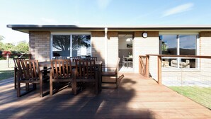 A modern house with a deck, a dining area with wooden furniture, and a large window.
