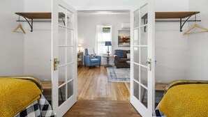 A hallway with a bed on the left, a blue chair, a brown sofa, and a lamp in the center. - Historic 2BR Prescott Home | Walk Downtown (Prescott)