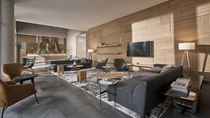 Ein modernes Wohnzimmer mit grauem Sofa, Ledersesseln, einem Couchtisch und einem an der Wand befestigten Fernseher.
