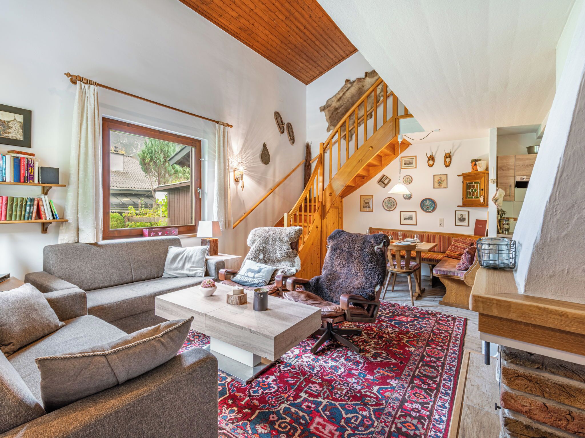 Een gezellige woonkamer met een houten trap, een bank, een bijzettafeltje en een kamerbreed tapijt.