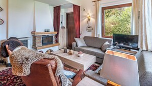 A cozy living room with a fireplace, a sofa, a television, and a dining area. - Landhaus Kunze by Interhome (Gröbming)