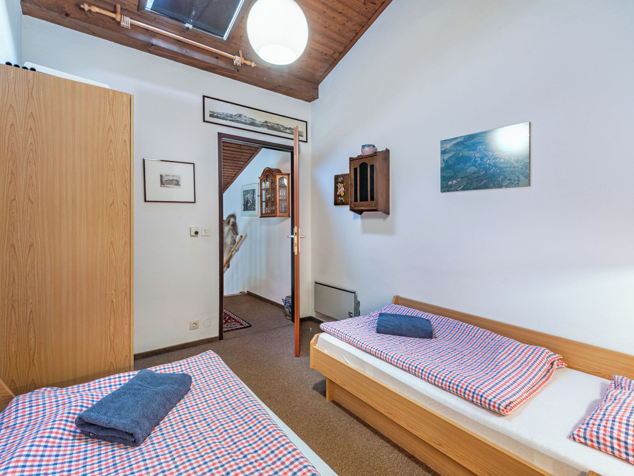 A room with two single beds, wooden wardrobe, a wooden ceiling, and a small cabinet.