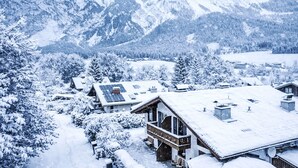 Eine verschneite Berglandschaft mit einer Lodge, deren Fassade aus Holz ist und Solaranlagen auf dem Dach hat.