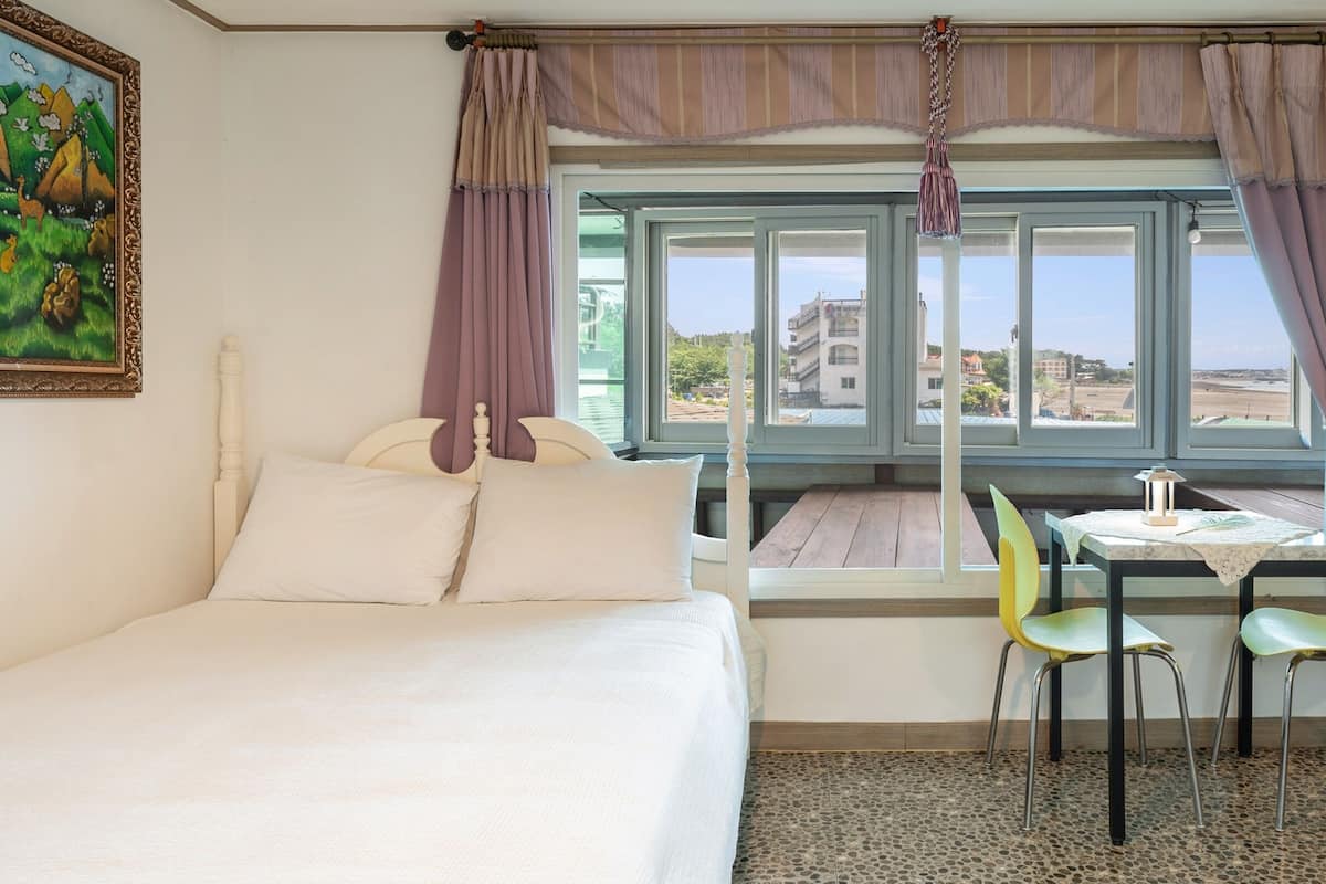 Habitació d'hotel amb un llit, una taula i cadires, una vista per grans finestres i un quadre a la paret.
