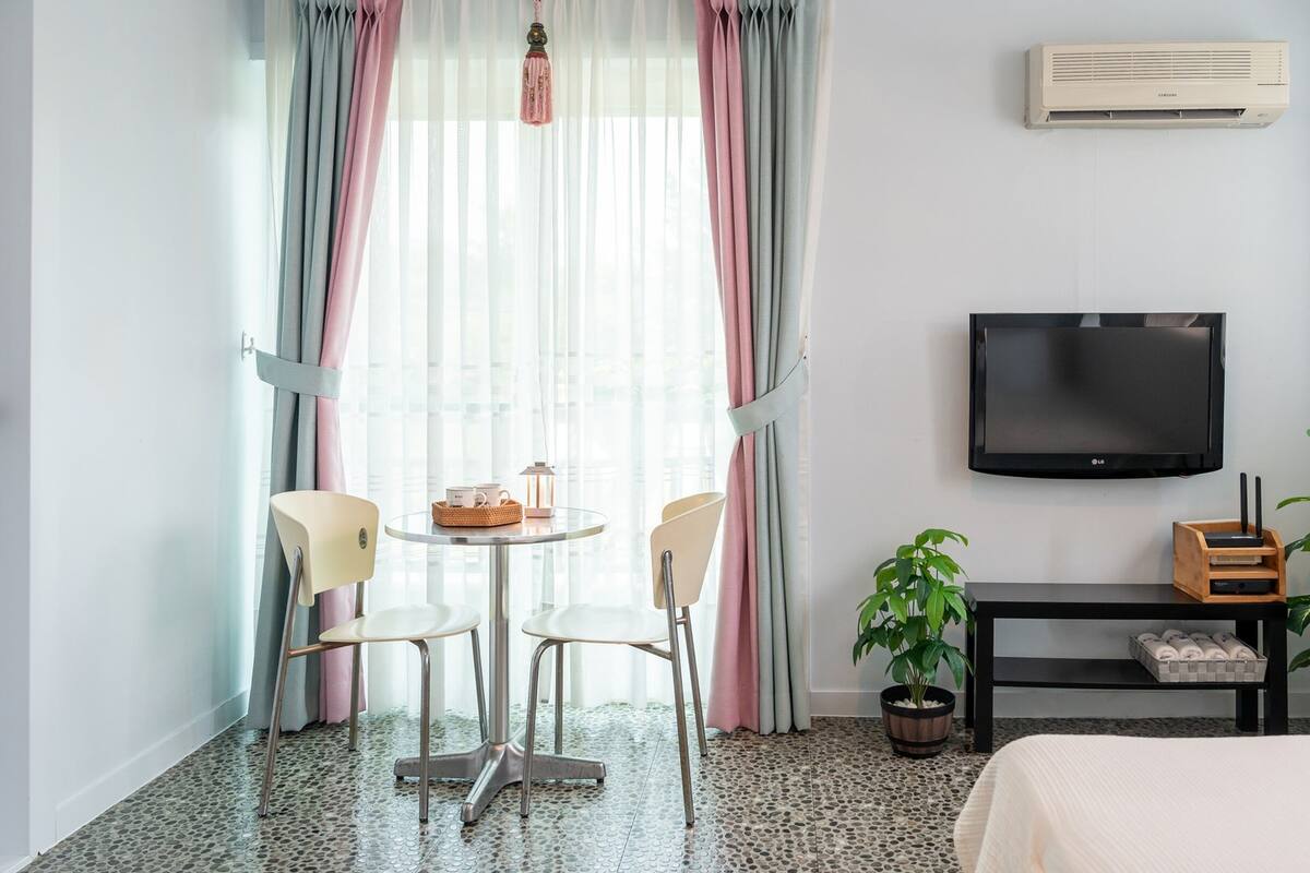 Habitació d'hotel amb un llit, una televisió, una taula petita amb cadires, una planta i un aire condicionat.