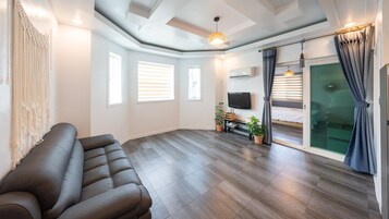 Una sala de estar moderna con un sofá, un televisor, una cama y un ventanal corredero.