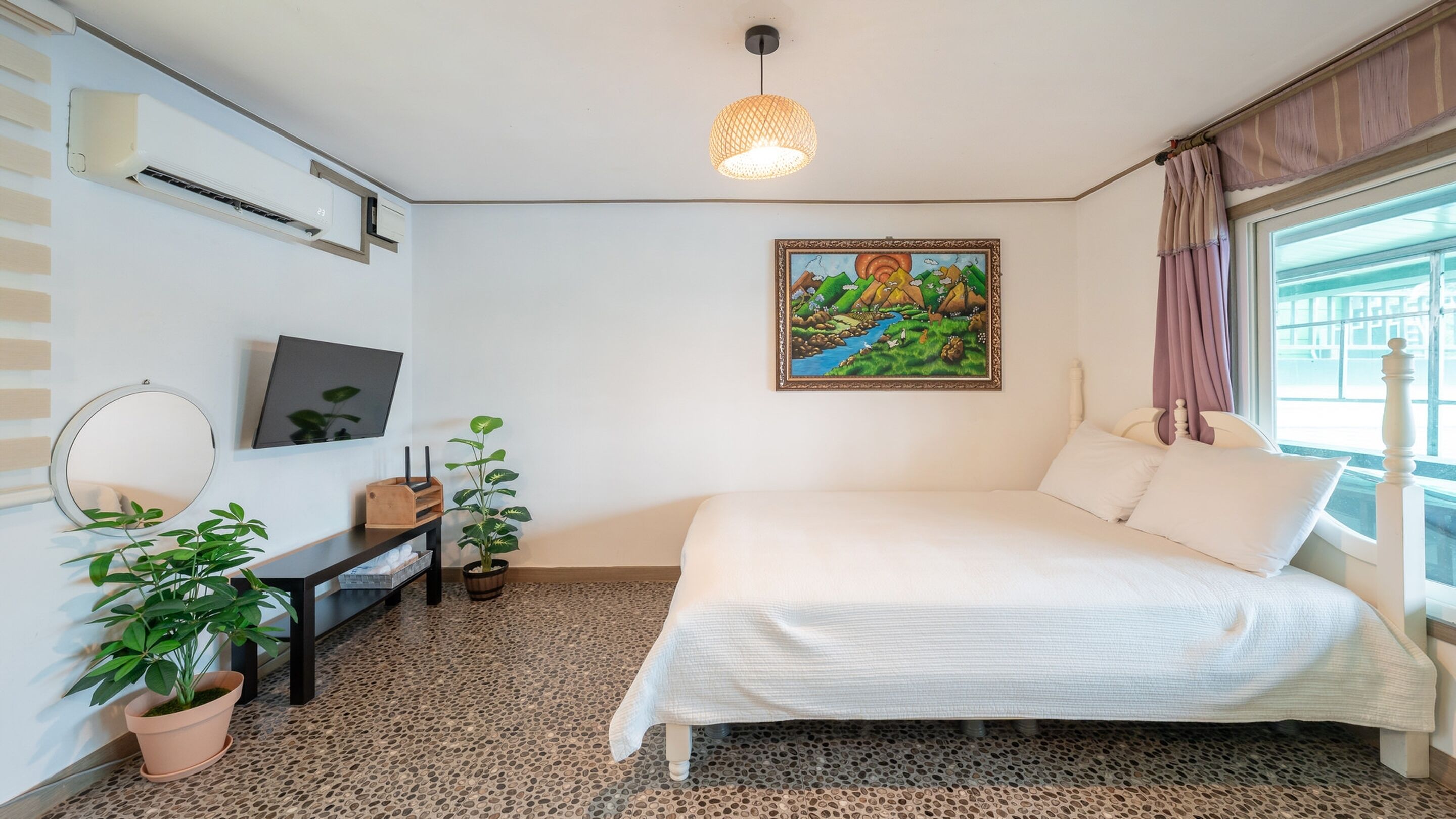 Un dormitorio con cama, escritorio, espejo, planta en maceta y un cuadro en la pared.