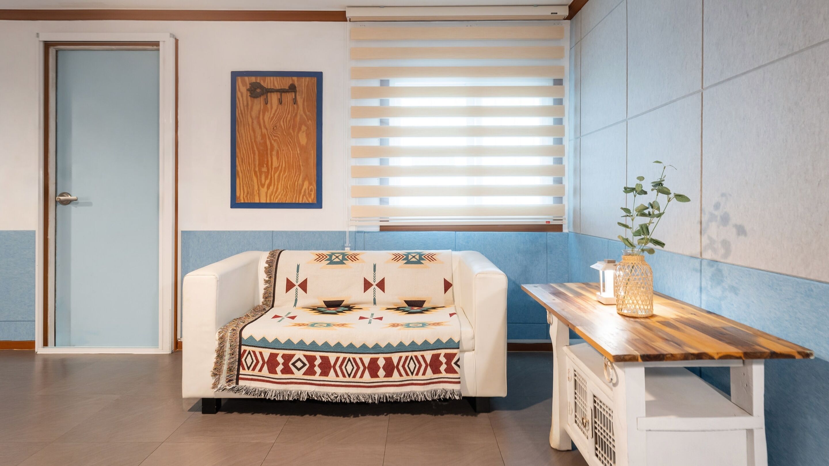 A room with a white sofa, a wooden table, a wall-mounted key, and a window with blinds.