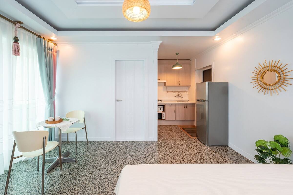 Habitació d'hotel amb un llit, una taula petita amb cadires, una cuineta i vista a la ciutat.