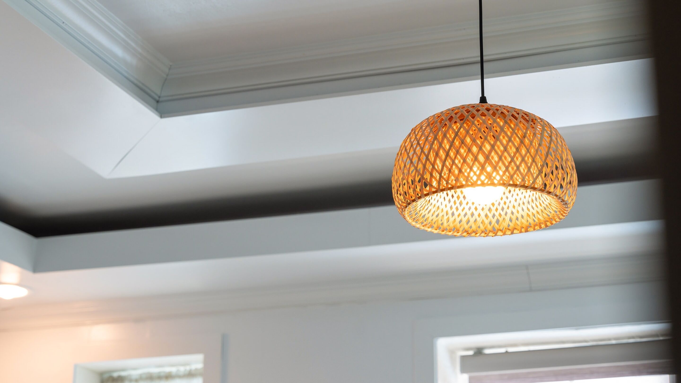 A hanging woven light fixture in a room with white walls and a sloped ceiling.