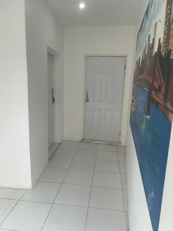 A hallway with white walls, a tiled floor, a white door, and a poster on the right wall.