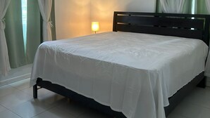 A bedroom with a bed, curtains, a ceiling fan, a wall-mounted lamp, and a tiled floor.