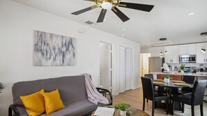 Un salon moderne avec un canapé gris, des coussins jaunes, une table basse en bois et un ventilateur de plafond.