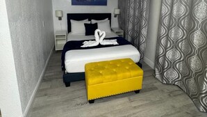 Ein Hotelzimmer mit Bett, Nachttisch, Lampe, einem Gemälde und einem gemusterten Vorhang.