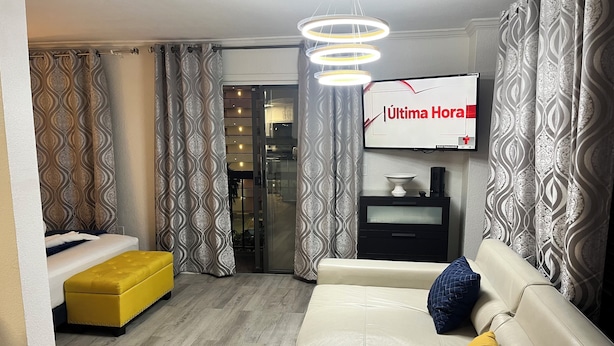 Ein modernes Wohnzimmer mit einer Couch, einem Hocker und einem an der Wand befestigten Fernseher.