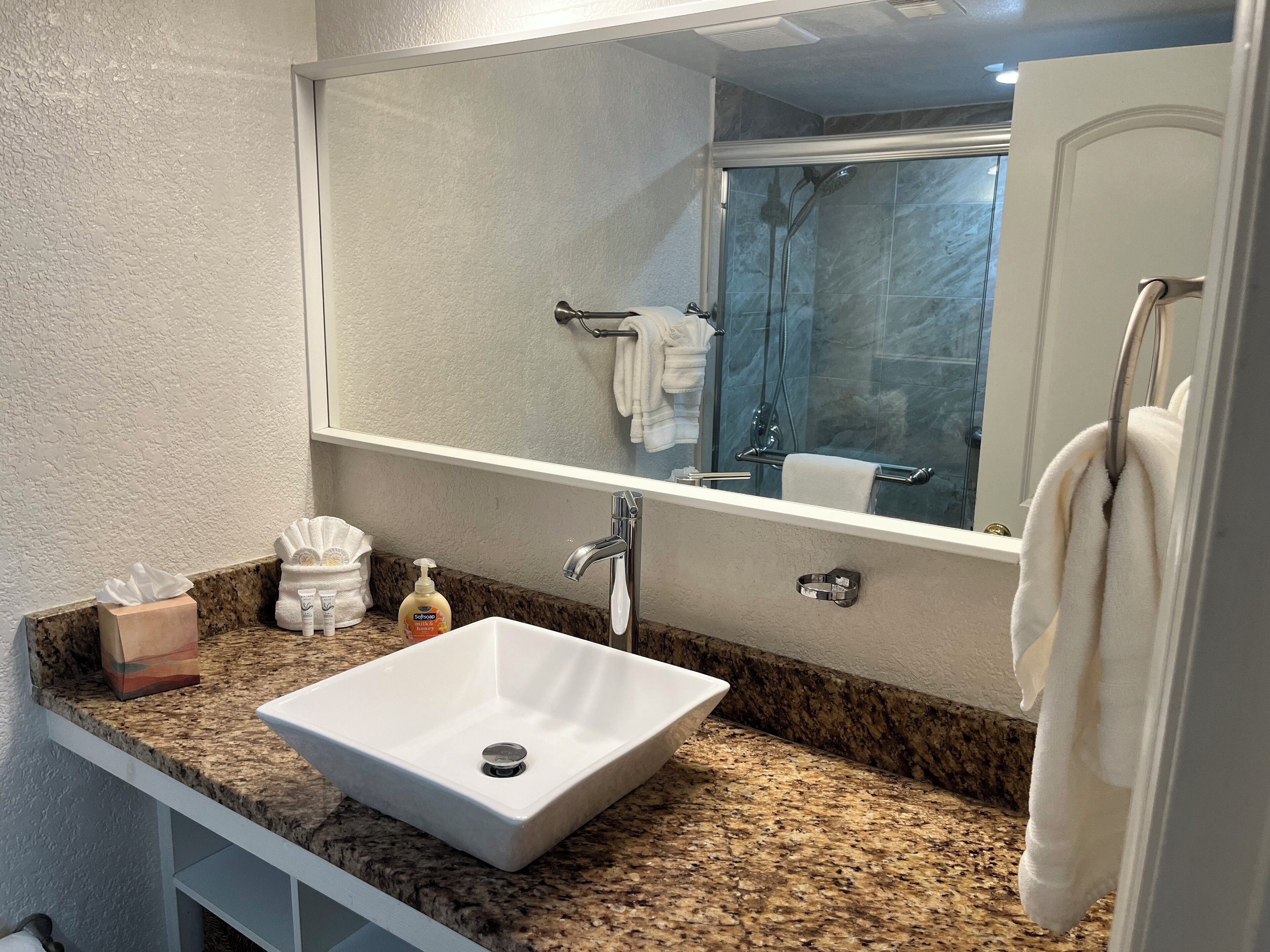 A bathroom with a white sink, granite countertop, and a large mirror above the sink.