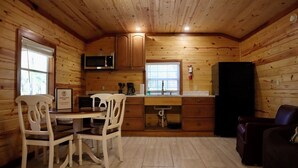 A compact kitchen with wooden walls, a microwave, a refrigerator, and a dining area with two chairs. - Charming Pondview Cabin (Andalusia)