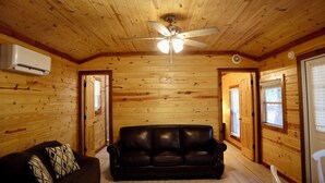A log cabin interior with a leather sofa, a ceiling fan, and wooden walls. - Charming Pondview Cabin (Andalusia)