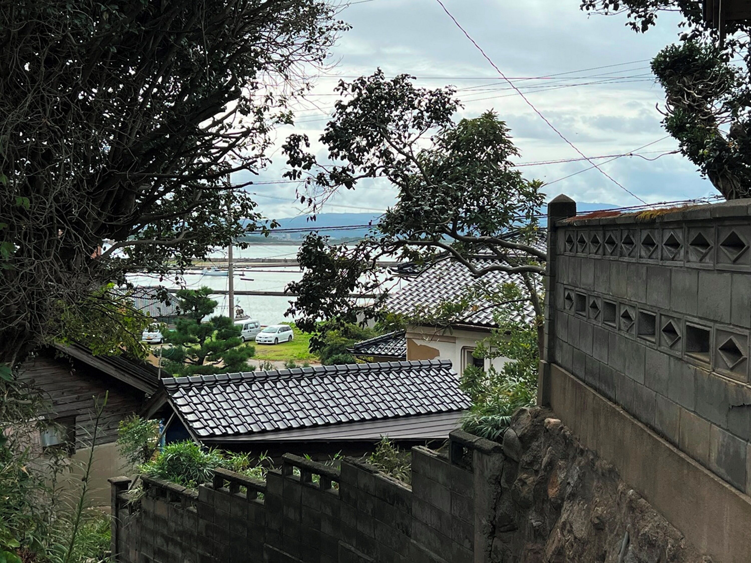A traditional Japanese house with a tiled roof, surrounded by greenery and a view of a body of water.