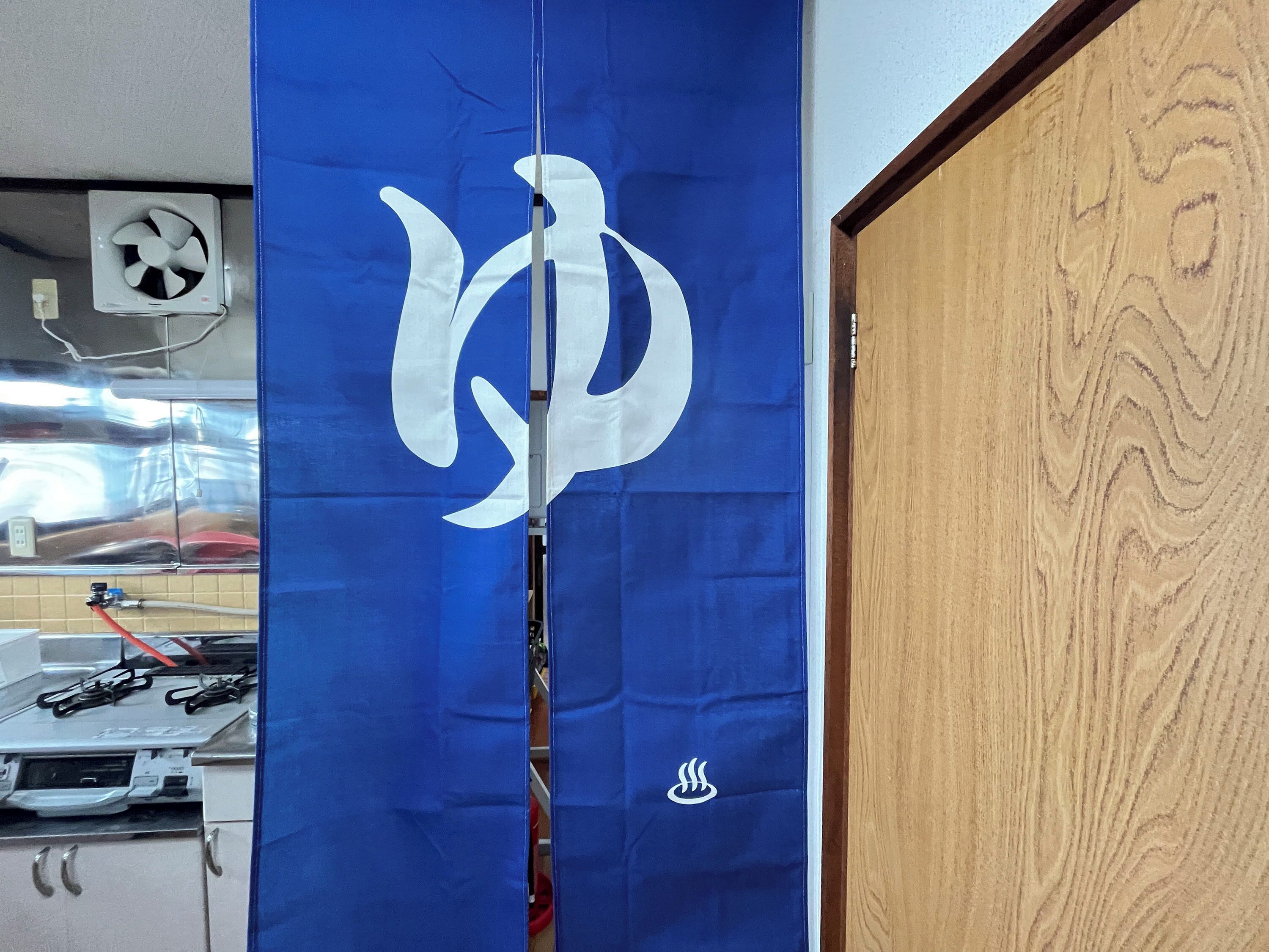 A blue curtain with a white logo, a wooden door, and a ceiling fan.