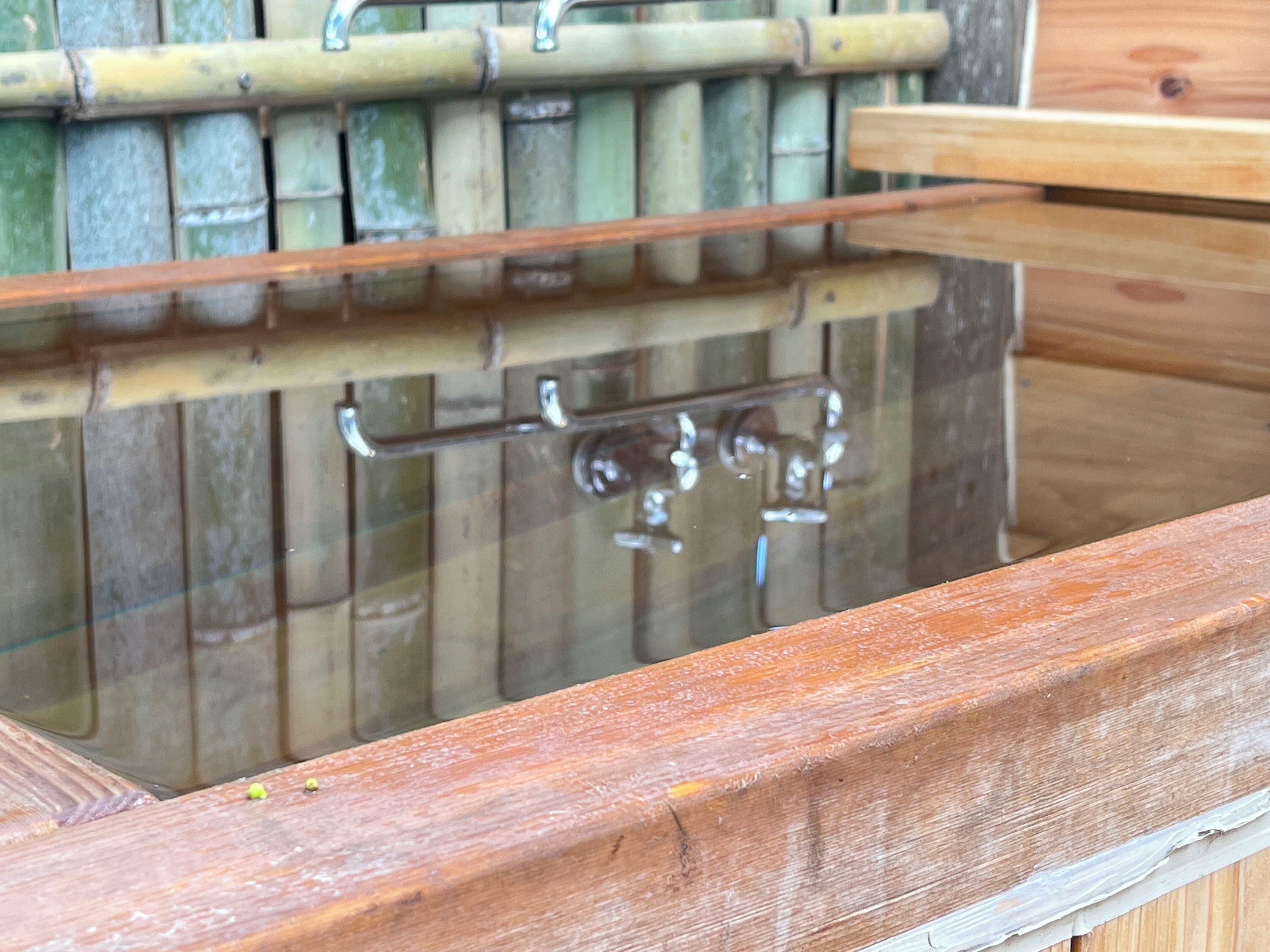 A wooden bench with a metal frame and a bamboo wall in the background.