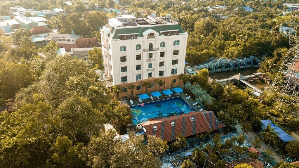 A large hotel with a central courtyard, a swimming pool, and a surrounding lush green area.