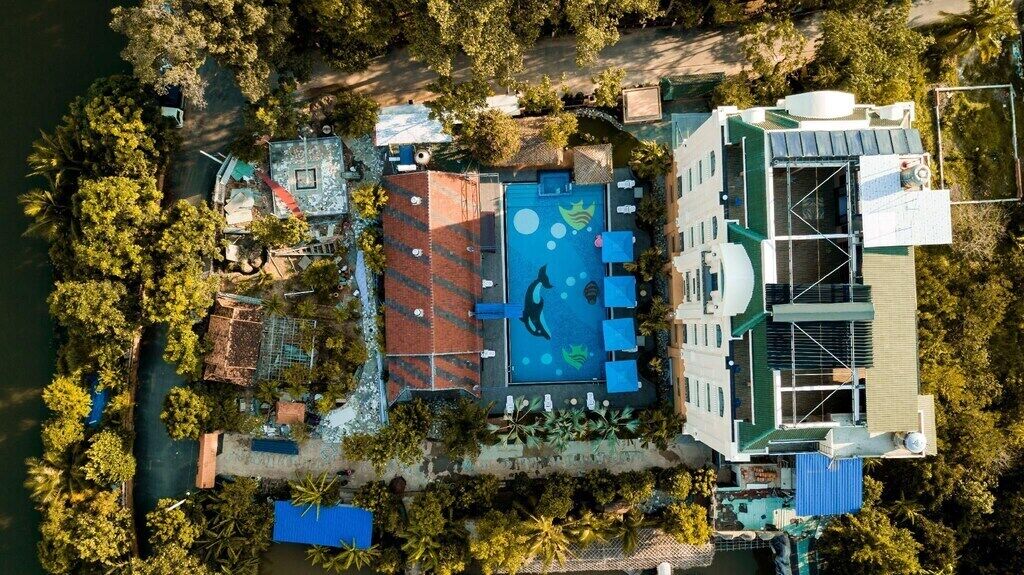 Vue aérienne d’un complexe hôtelier doté d’une piscine, d’un bâtiment surmonté d’un toit végétalisé et entouré de végétation.