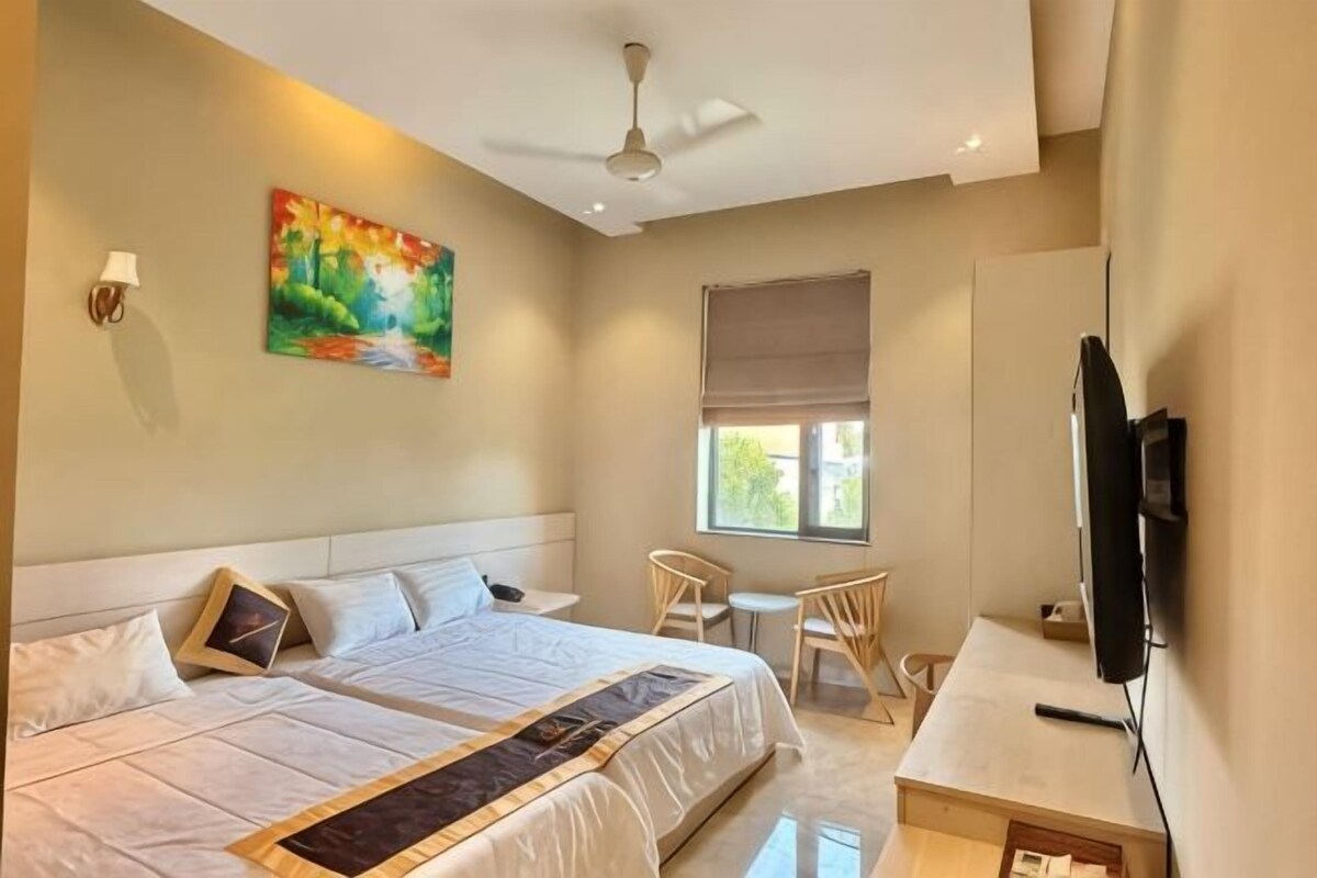 A hotel room with a bed, a desk, a chair, a television, and a painting on the wall.