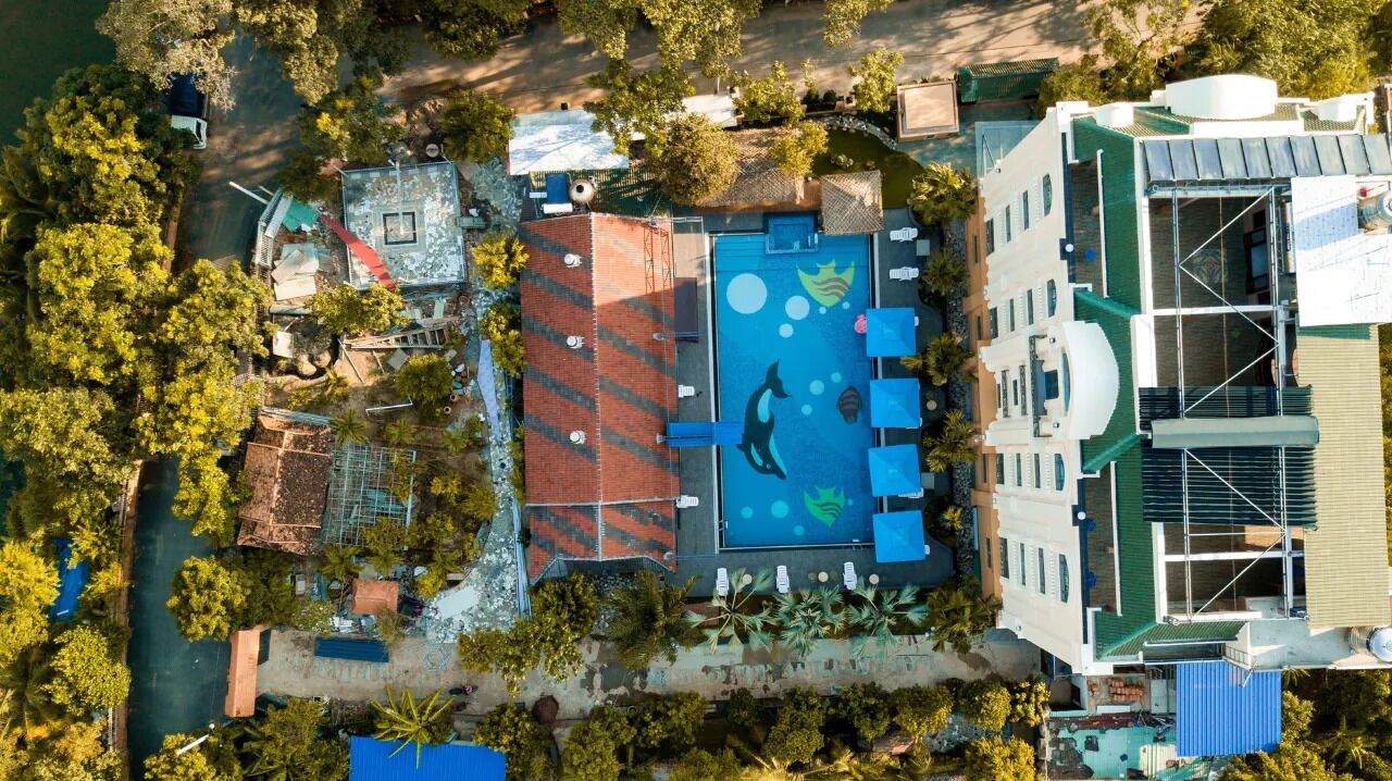 An aerial view of a hotel with a swimming pool, a covered area, and a building with a green roof.