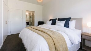 A hotel room with a bed, bedside table, lamp, and a door leading to a bathroom.