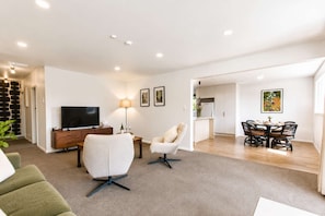A modern living room with a TV, sofa, armchair, and dining area with a table and chairs.