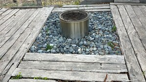 A metal grill on a wooden deck surrounded by pebbles.